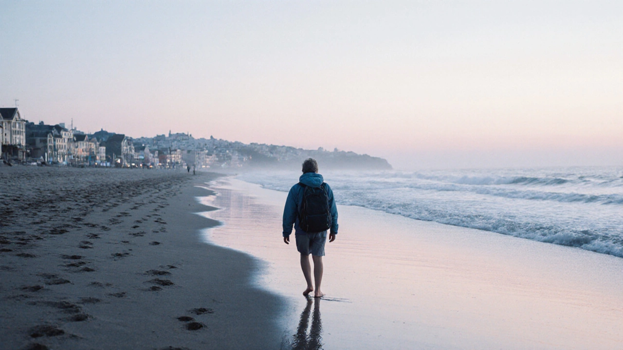 Una persona camina descalza por una playa al amanecer, dejando huellas que se borran con la marea.